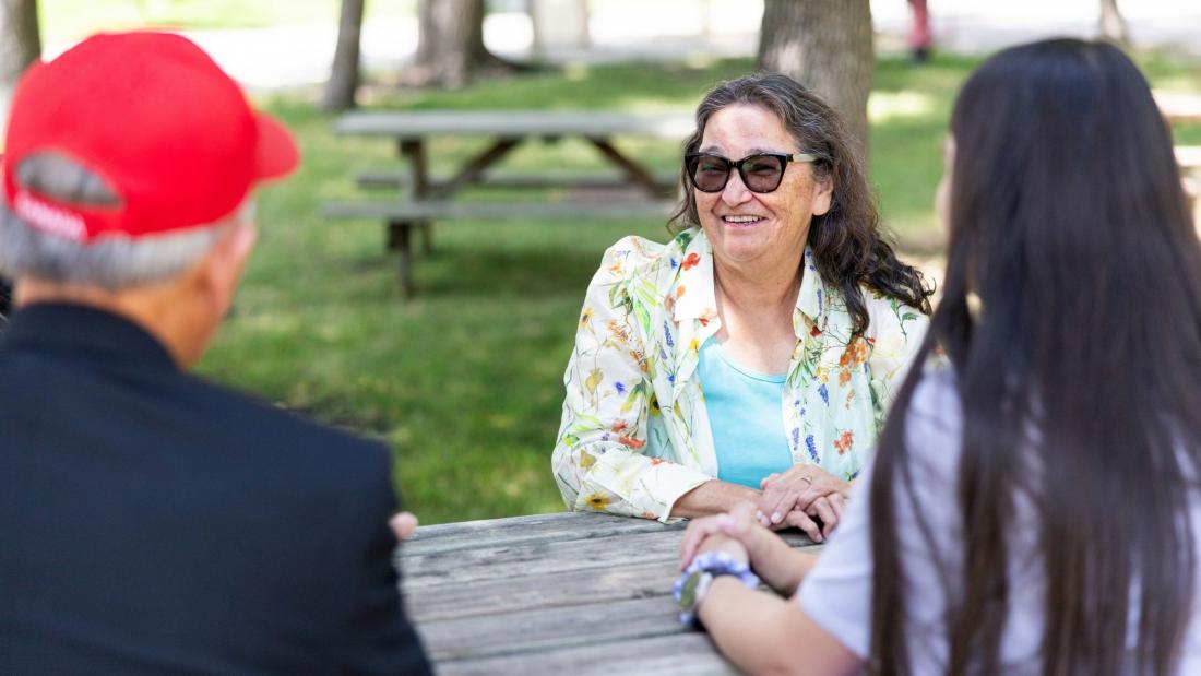 Grandmother-in-Residence sitting outside at a picnic table talking to a student.