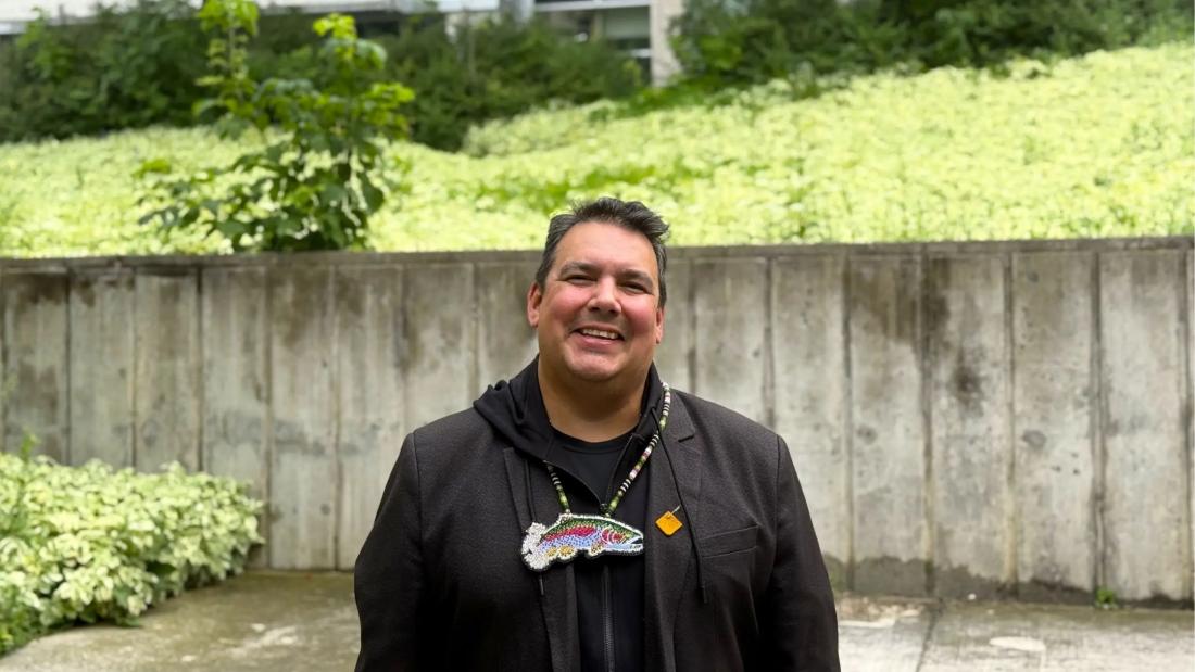 Professor Niigaan Sinclair stands outside and smiles at the camera.