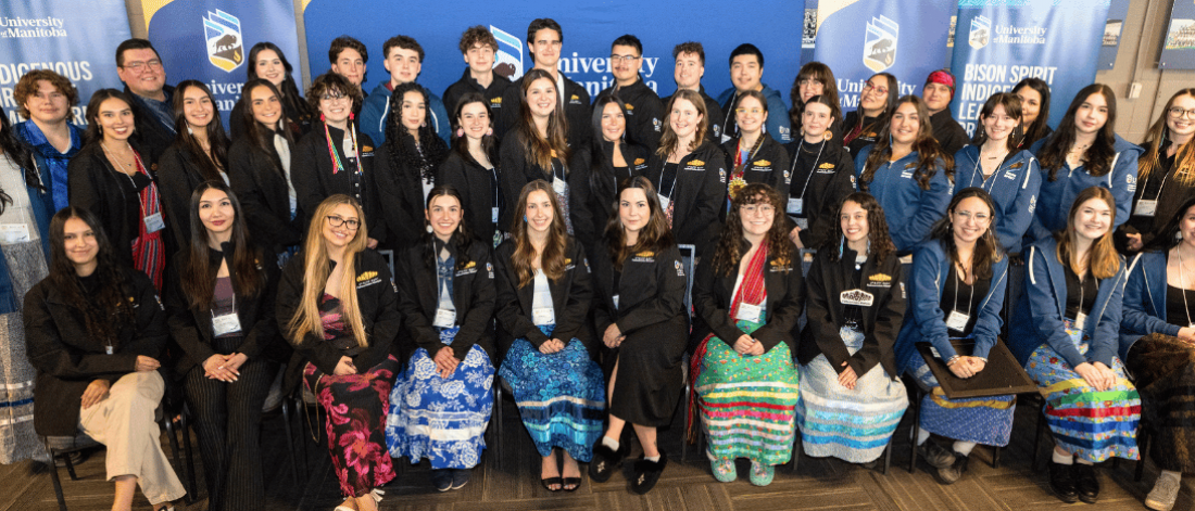 Group photo of University of Manitoba Indigenous leadership program participants and staff at a campus event, standing and seated in front of program banners.