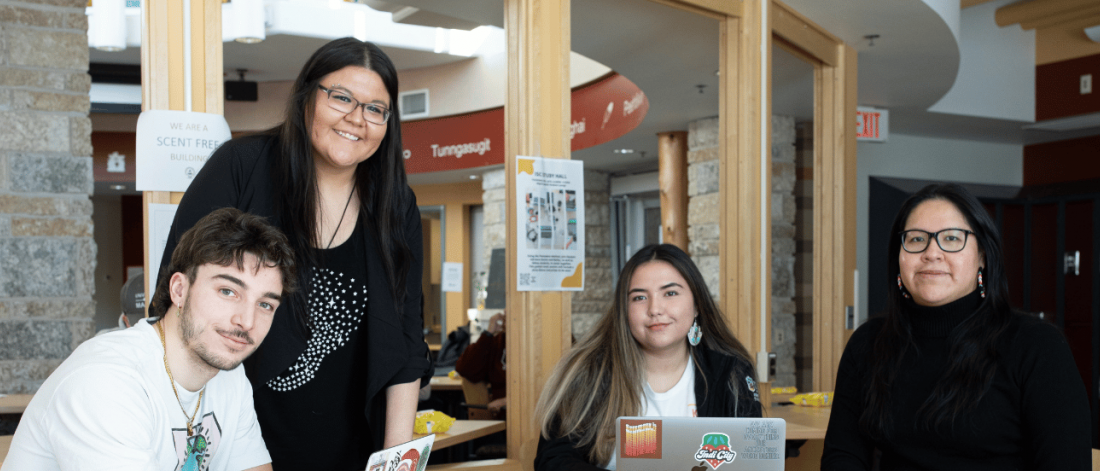 Four Indigenous students and staff gathered at the Indigenous Student Centre, smiling around a table in a welcoming campus space.