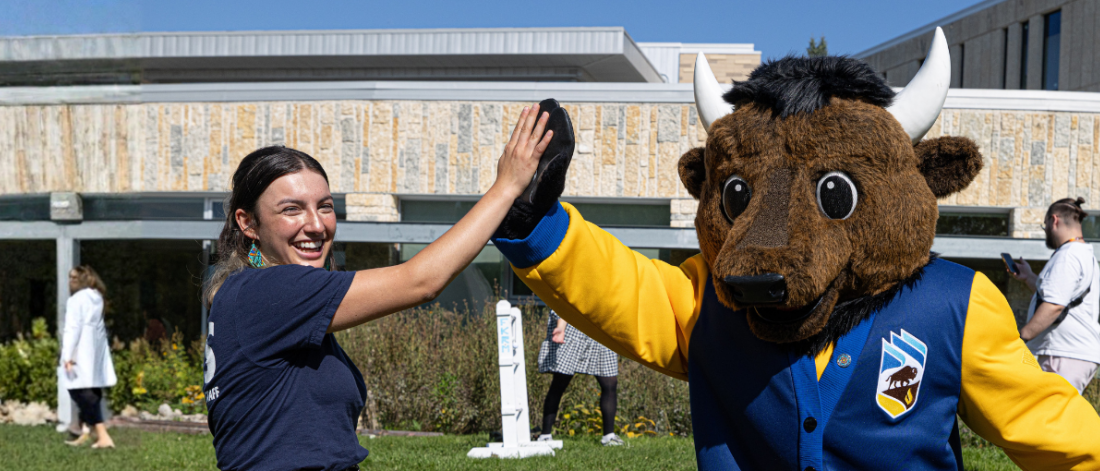 A student high-fives Billy the Bison outdoors.