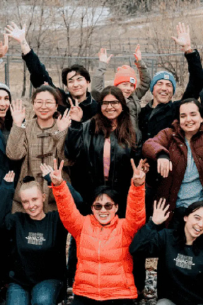 Group of students and community members outdoors, smiling and waving together during a gathering or retreat.