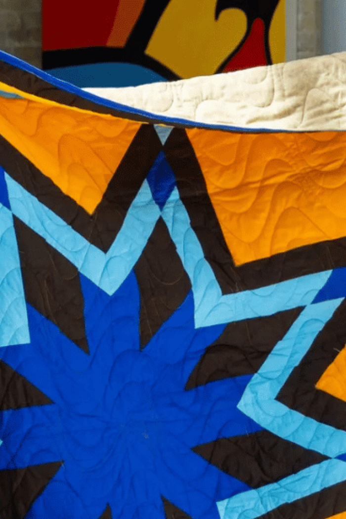 Two people hold up a brightly coloured star-pattern quilt during the Honouring the Indigenous Campus Community ceremony at the University of Manitoba.