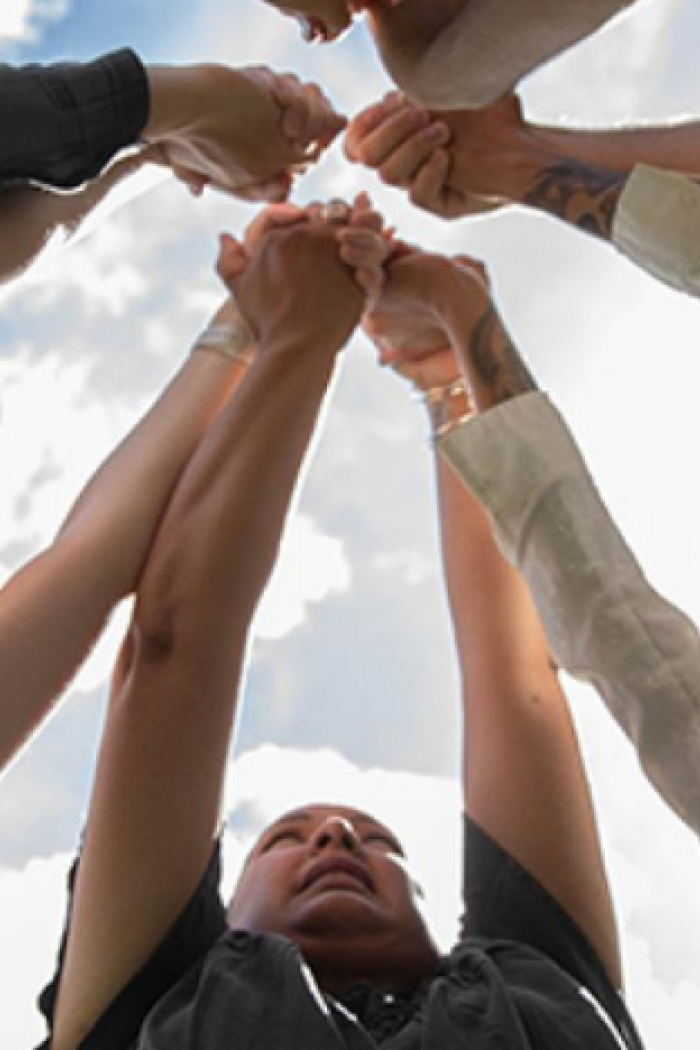 Students standing in a circle with their hands joined together outdoors.