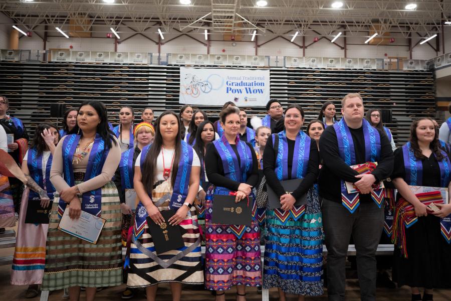graduates proudly standing with their stoles at pow wow