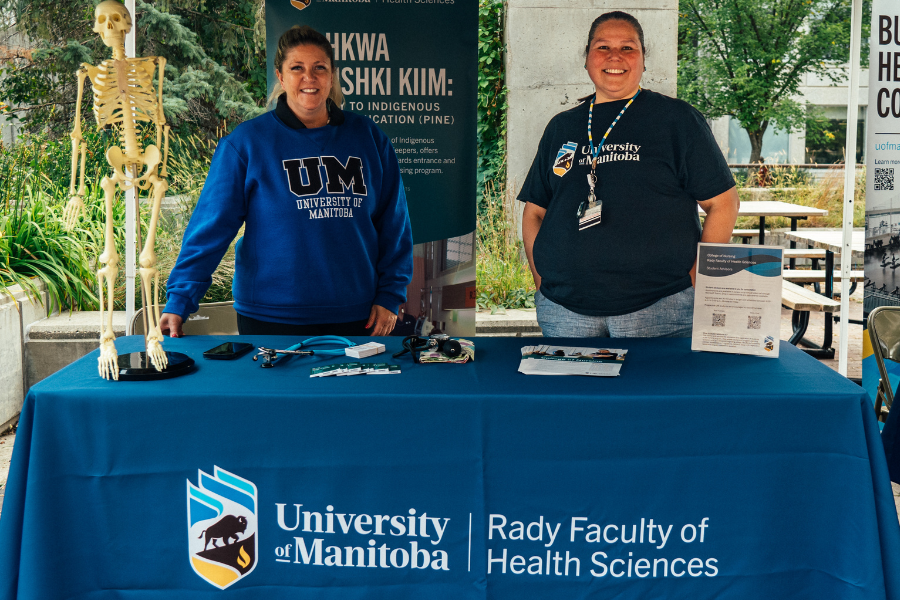 Two staff at a Rady Faculty of Health Sciences booth with medical tools and a skeleton model.