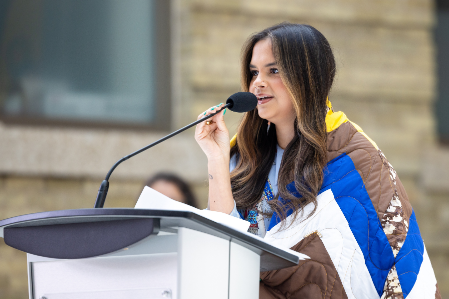 Woman wrapped in a star blanket speaks at the podium.