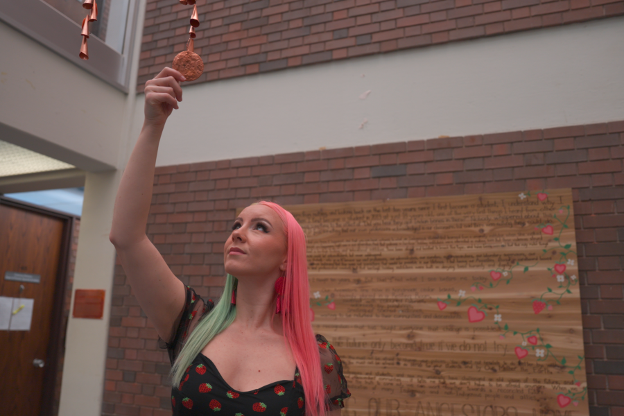 female reaches for copper jingles hanging from atrium.