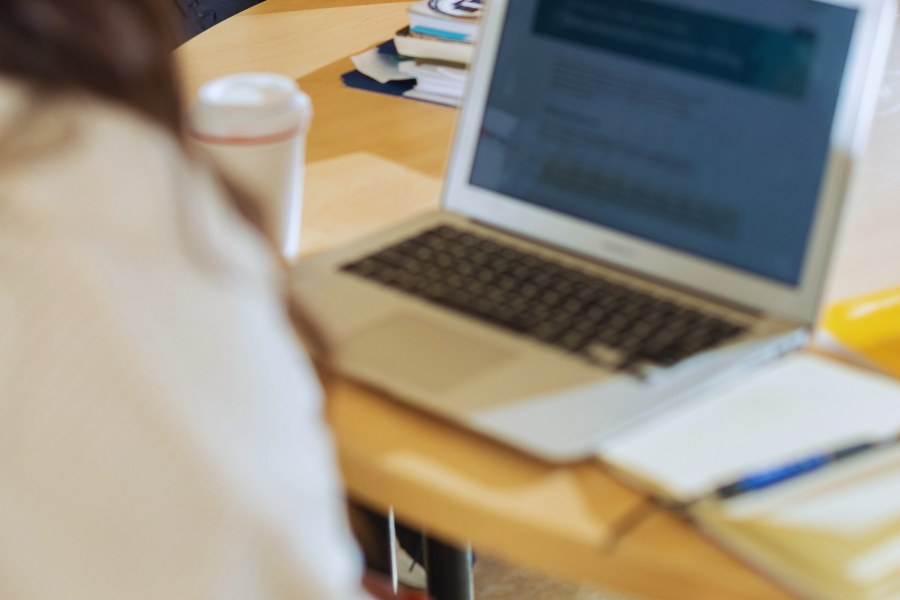 Person working on a laptop at a table with a notebook and coffee nearby.