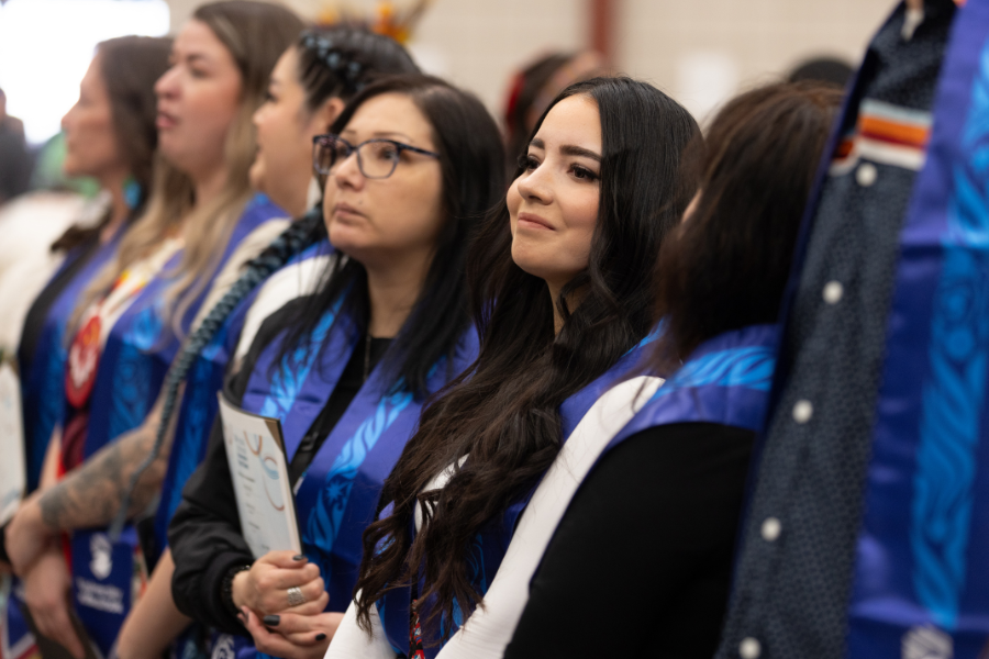 Indigenous graduates wearing blue stoles at a graduation pow wow