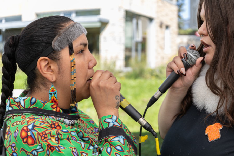Two performers singing into microphones outdoors.