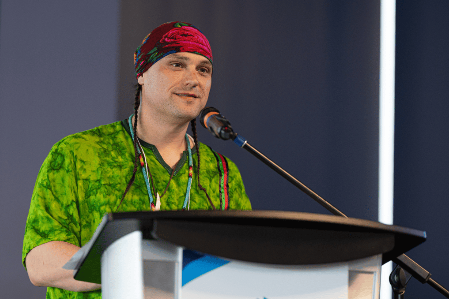 A speaker wearing colourful clothing delivers remarks at a podium.