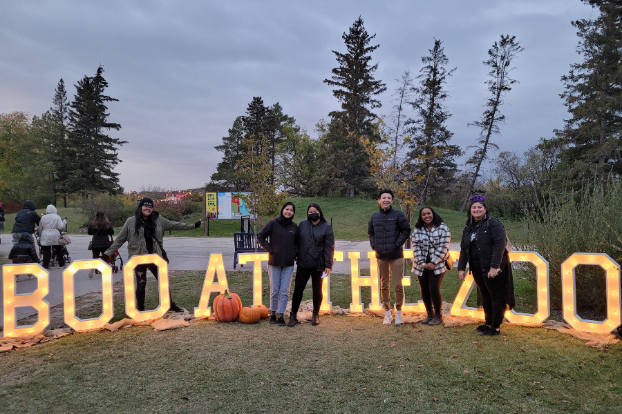 Students pose by an illuminated “Boo at the Zoo” sign.
