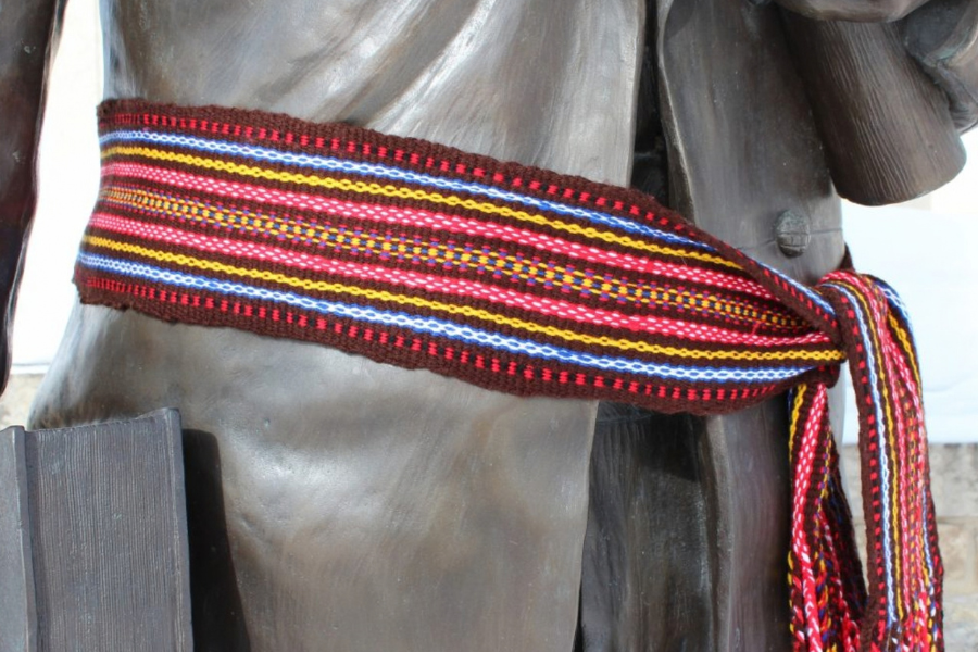A colourful Métis sash tied around the waist of a statue.