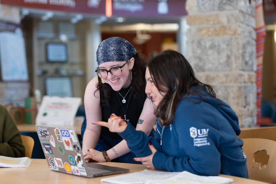 Two students smile and look at a laptop together.