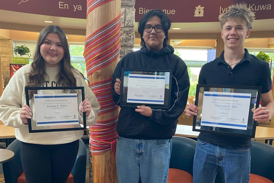 Three students stand inside holding certificates.