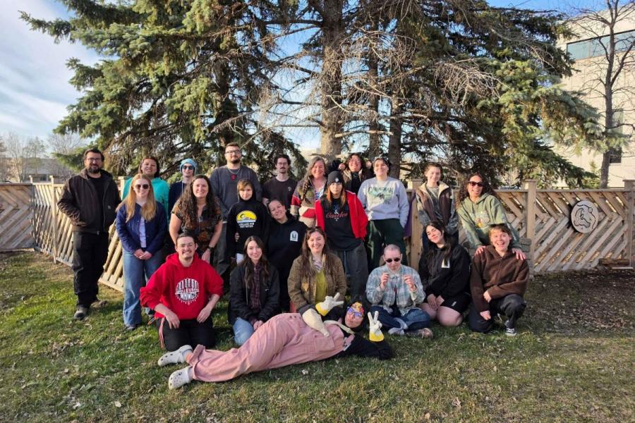 A group of people pose outdoors in front of a large tree on green grass.