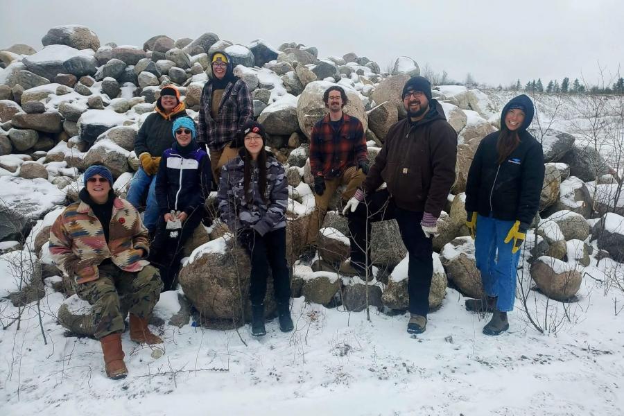 A group stands outside in the winter in front of large rocks, smiling at the camera.