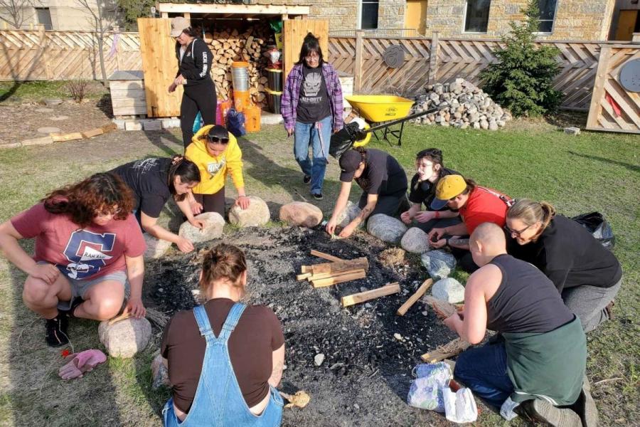 A group of people work together to build a fire in an outdoor area.