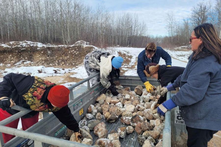 People gathering rocks into a cart outdoors in the winter.