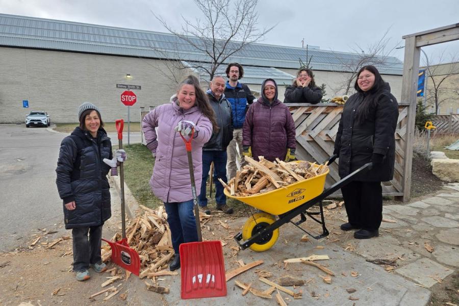 A group with shovels and a yellow wheelbarrow filled with wood pose for the camera.