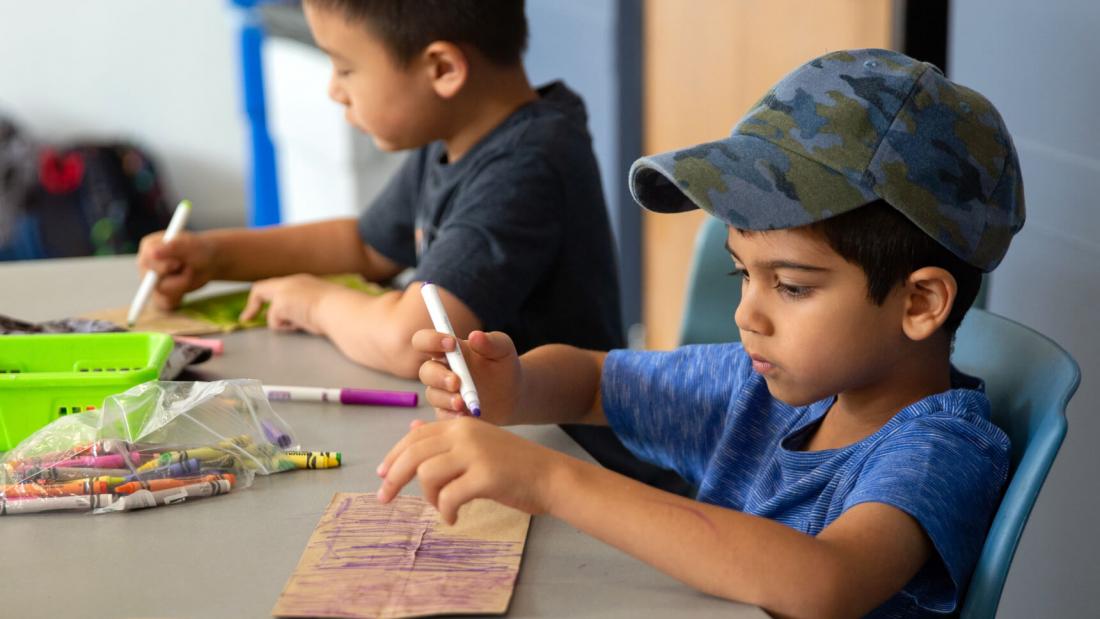 A mini-u child colours at a table. 