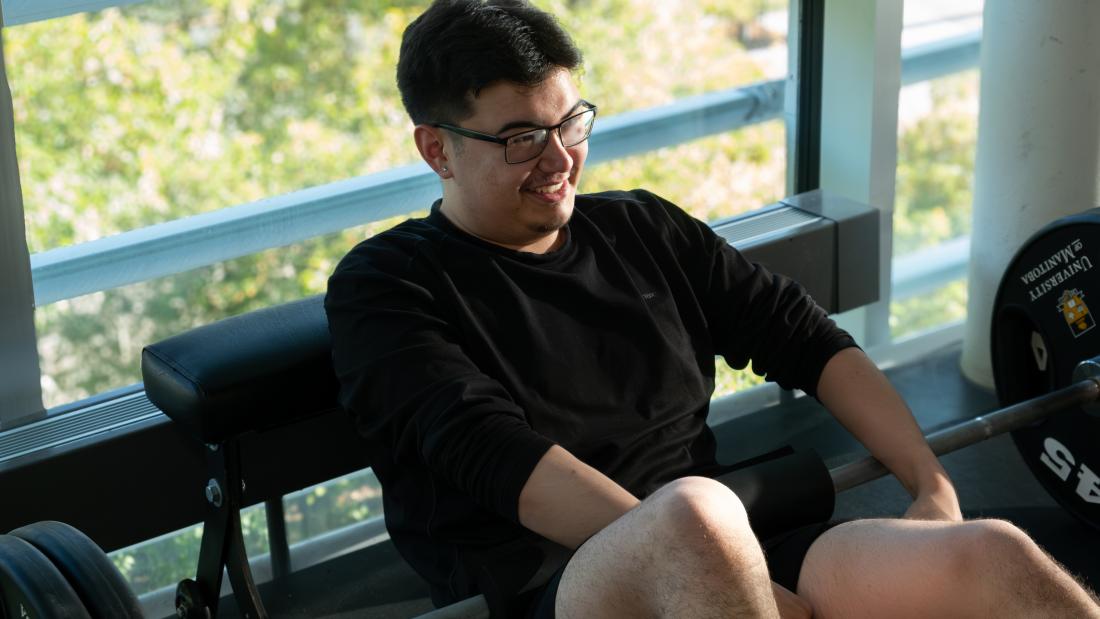 A gym member smiling while sitting on the ground with a weight across his legs