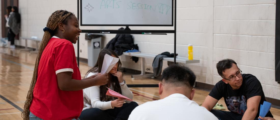 A group of students sitting on the gym floor working on a project