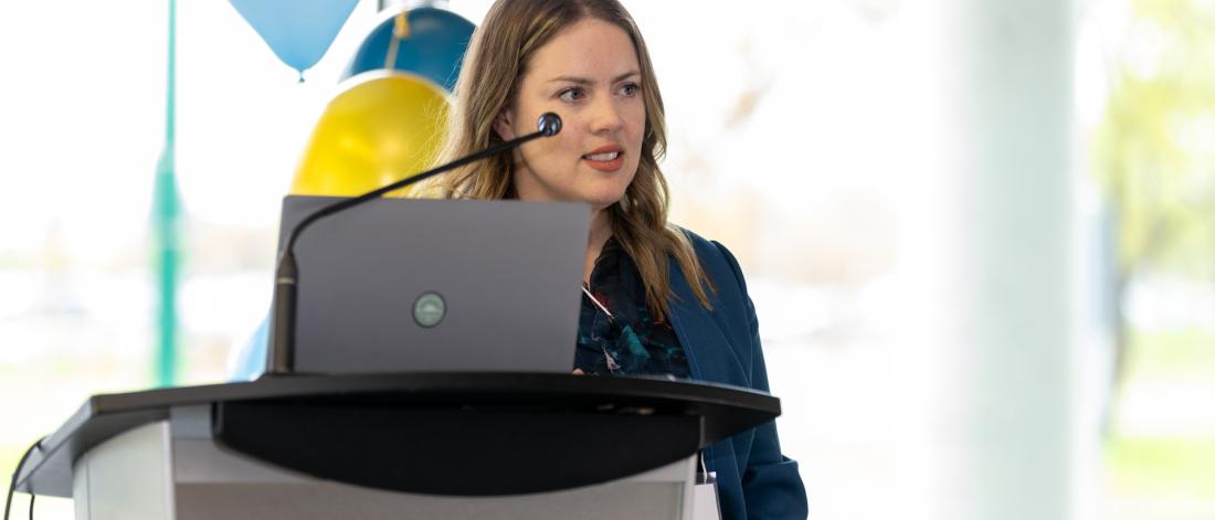 Dr. Heather Gainforth stands behind a lecturn and laptop while presenting