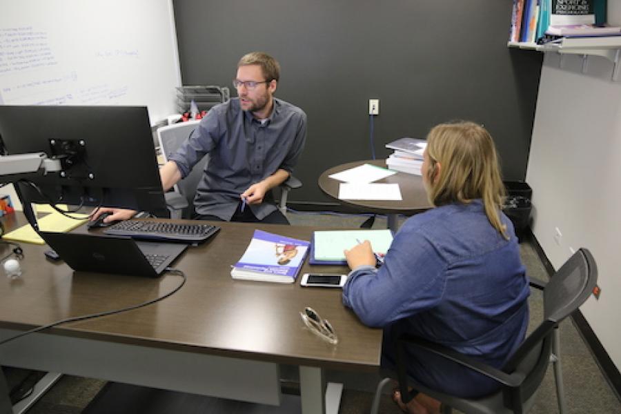 researcher talks with student at desk