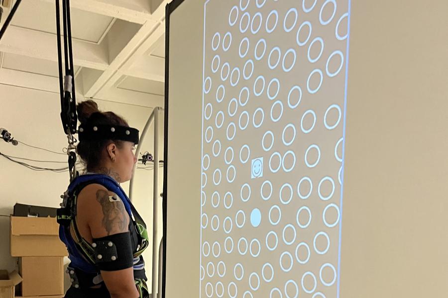 A woman standing in a harness viewing a screen with many circles on it during a lab test