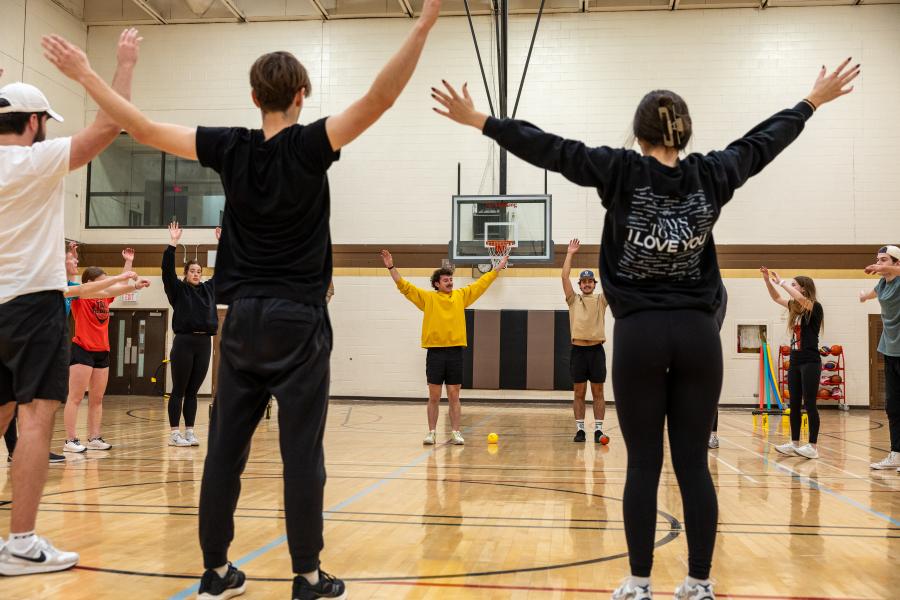 Students standing in a circle with their arms stretched out in a gym