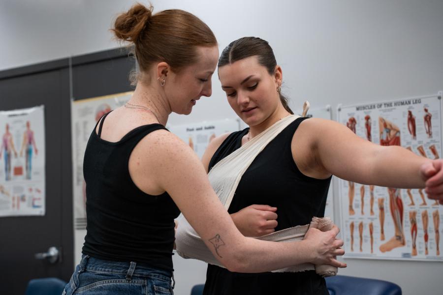 A student wrapping another students arm in a sling during a class demonstration