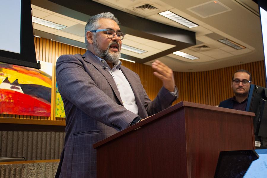 a bearded man in grey suit jacket and white shirt speaks at a podium in Robson Hall's moot courtroom