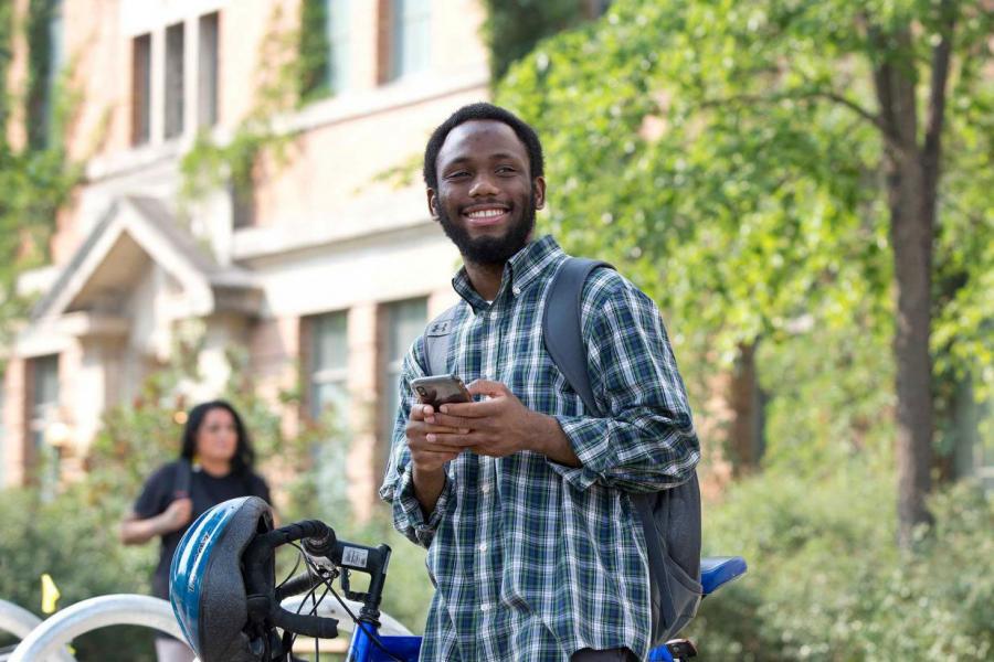 A man holding a cell phone near a bicycle on a university campus.