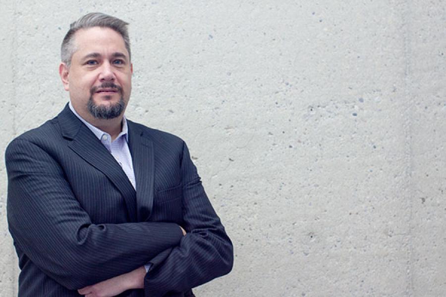 a man in a blue suit jacket stands arms crossed in front of a concrete wall
