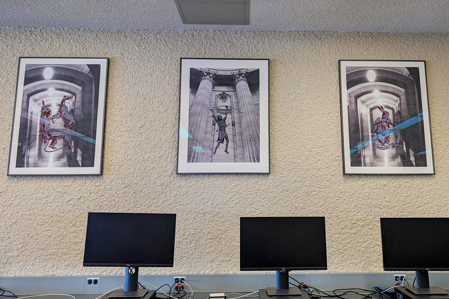 3 framed art pieces on a wall, photos of the legislature with graphics of Indigenous men hunting overlayed