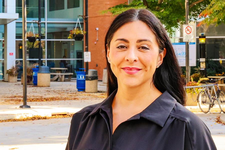 Dr. Amanda Fowler-Woods standing outside on a sunny fall day with the University of Manitoba Bannatyne campus in the background