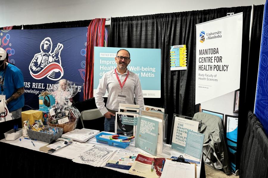 Dr. Nathan Nickel smiling and working behind the MCHP booth, surrounded by signs and documents.