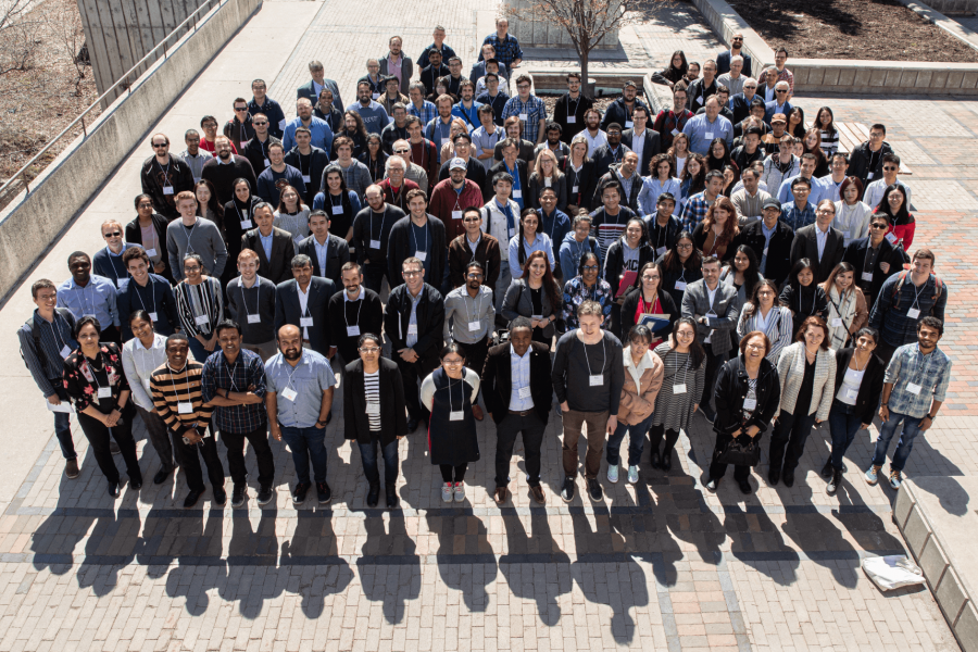 A large group of attendees from the 2019 Manitoba Materials Conference gather together outdoors for a group photo.
