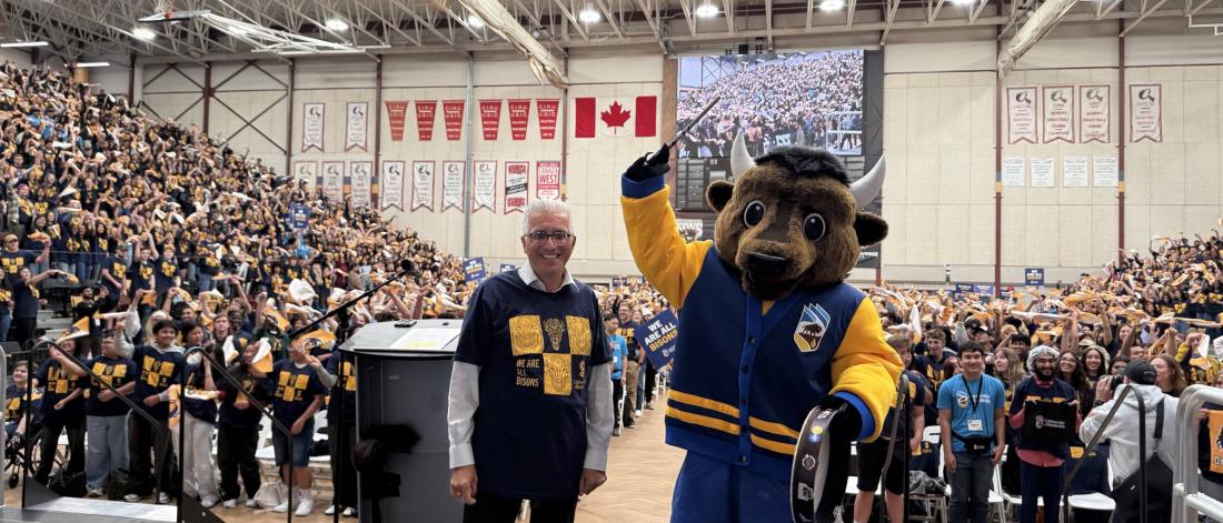 An image of president Michael Benarroch with UM mascot Billy the Bison in a gym with students.