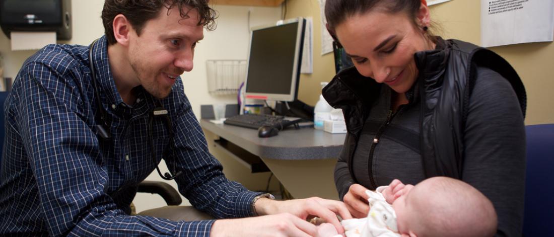 A caregiver holding an infant as the doctor does an assessment.