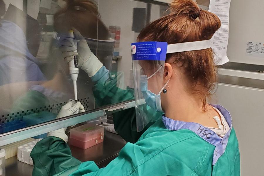 a researcher in protective equipment working with a specimen and pipette in a lab.
