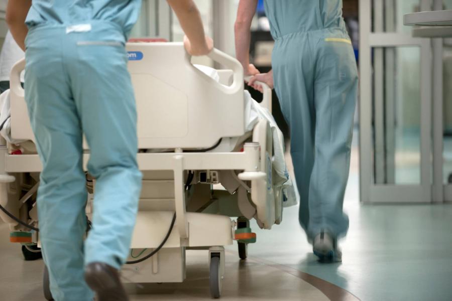 Two people rush to push a gurney down an emergency department hallway.
