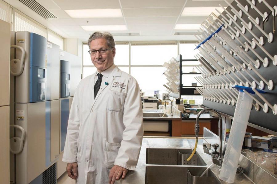 Researcher Charles Bernstein stands in a lab wearing a white lab coat. 