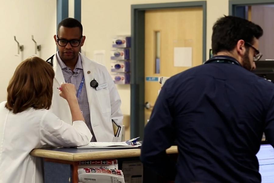 Medical staff stand at a desk speaking with each other.