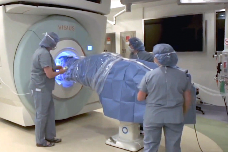three healthcare workers load a patient into a scanner.