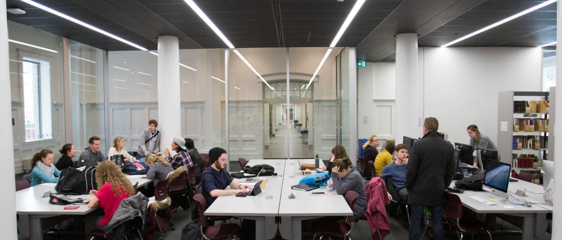 Students study and work at rows of tables in the seating area of the music library. 