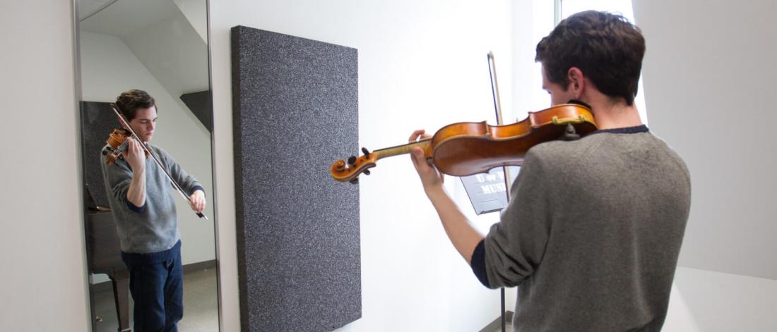 A student practices the violin in a practice room. 