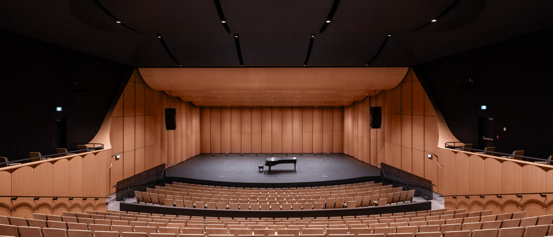 interior image of the Desautels concert hall. The hall is empty, with a piano in the centre of the stage.